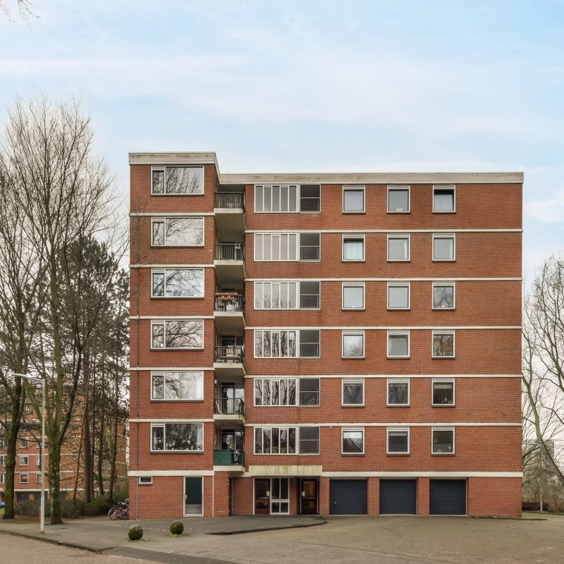 A multi-storey brick building standing apart from all the others surrounded by trees