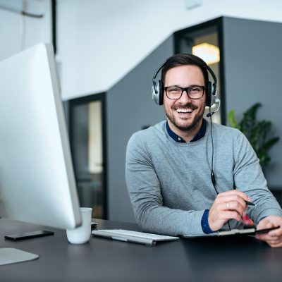 Agent taking notes while talking with customer using headphones and microphone in customer support center.